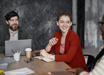 a woman in red talking to 2 people at a table with coffee