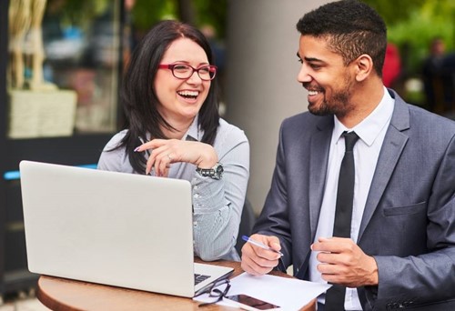 two happy finance professionals working outside with a laptop