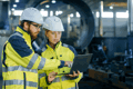 two construction workers pointing at a laptop in a manufacturing plant