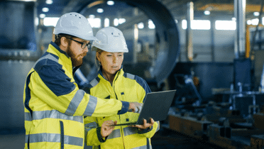 two construction workers pointing at a laptop in a manufacturing plant