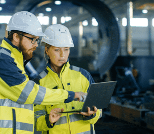 two construction workers pointing at a laptop in a manufacturing plant