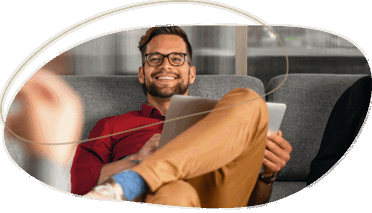 man in a red shirt smiling while sitting on a couch holding a laptop